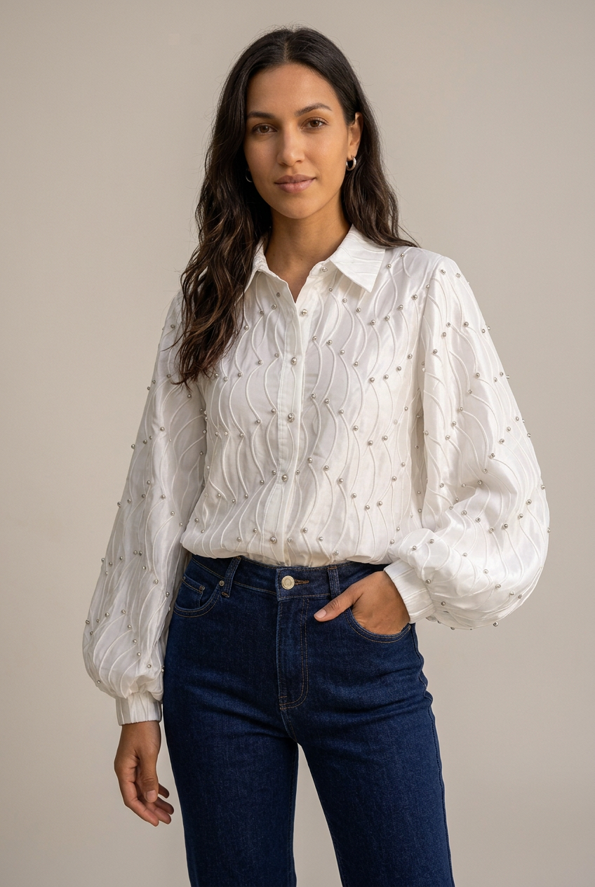 Celeste white embellished wave-pleated blouse styled with dark-blue jeans in a studio setting